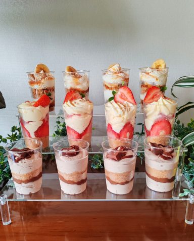Verre de desserts à couches avec fruits et crème sur un support en verre.